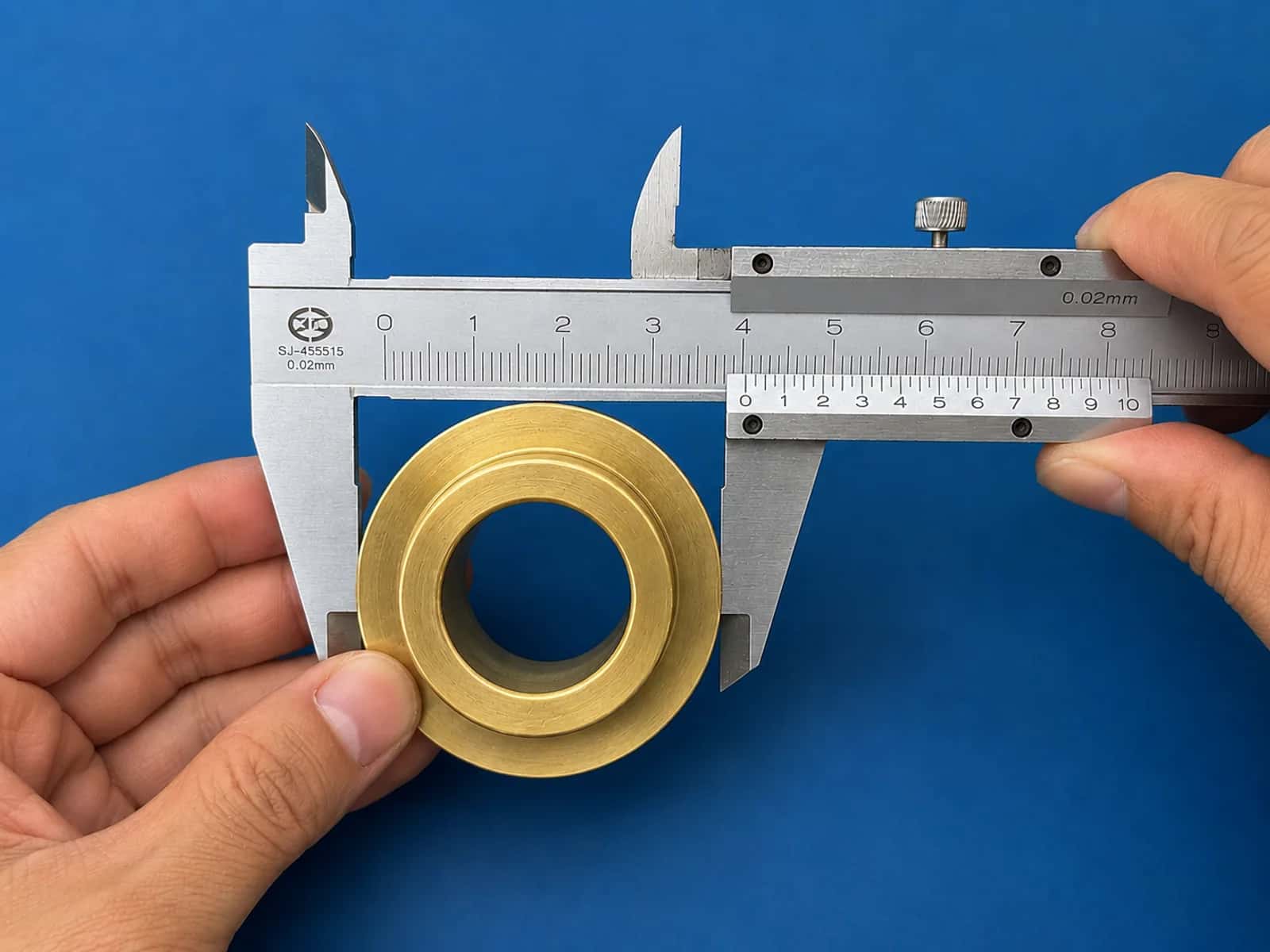 Hands using a vernier caliper to measure the outer diameter of a brass machined part