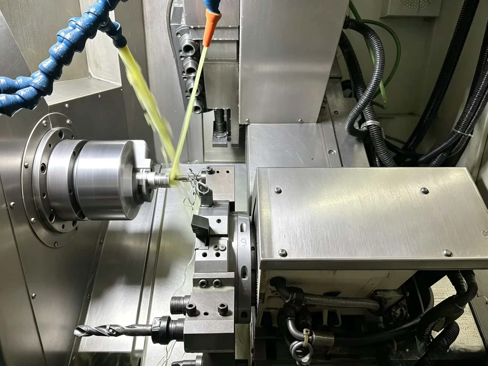 CNC lathe turning a steel workpiece with dual yellow-green coolant streams and a tool turret nearby