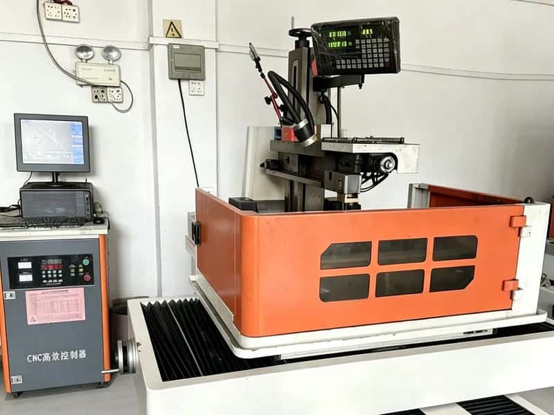 Wire EDM machine with orange tank and digital controls in a workshop