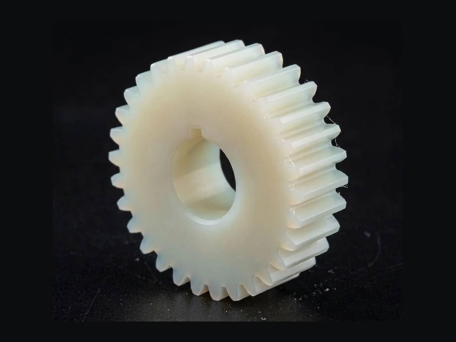CNC-machined nylon spur gear with a keyed bore on a dark work surface